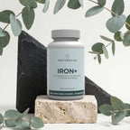 Żelazo w kapsułkach Naturecan Iron+ z 18 mg bisglicynianu żelaza, 60 porcji, na dekoracyjnym tle z liśćmi.
